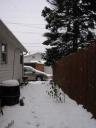 Side yard with snow on ground and falling.